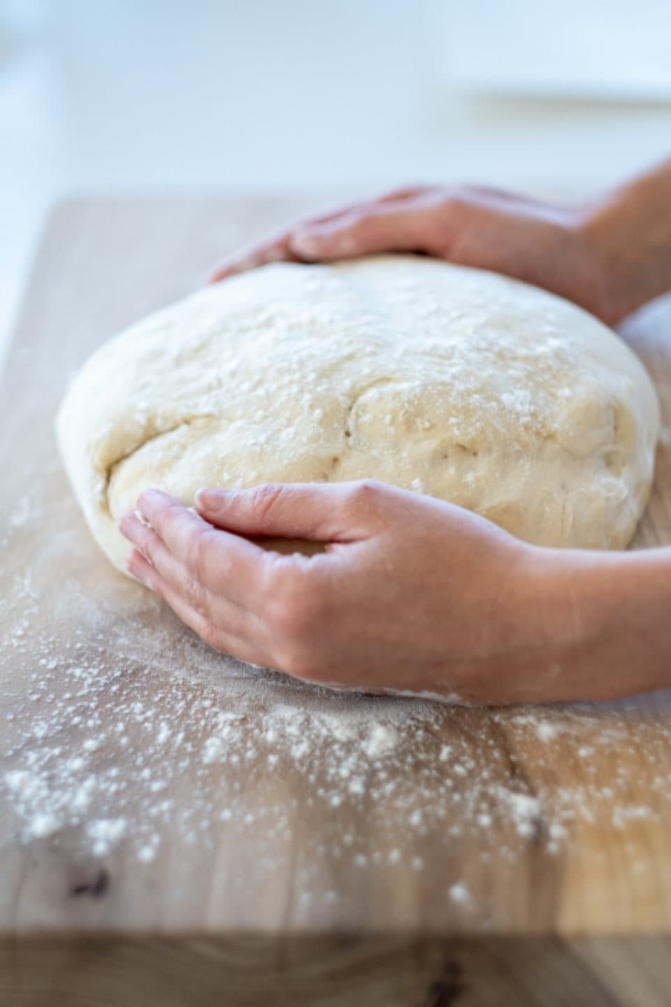A baker's hands shaping a round of dough on a floured board